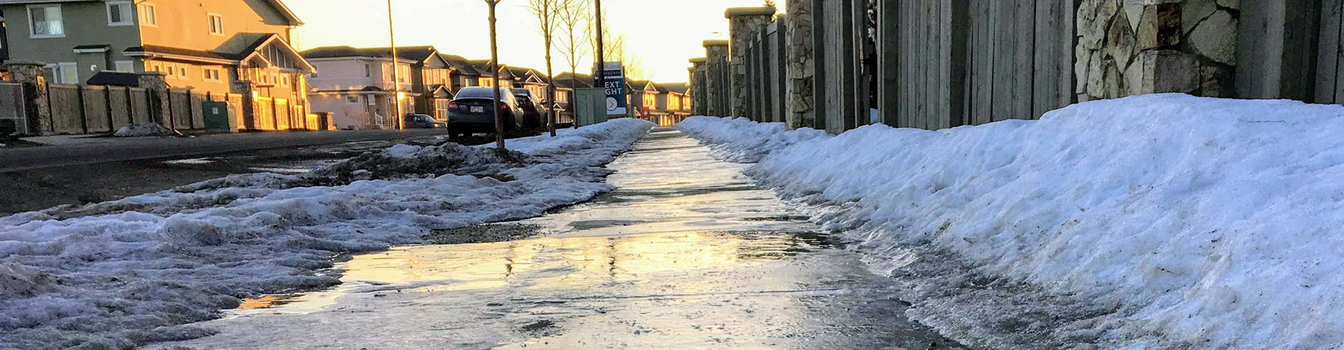 a closeup view of slippery black ice covering a sidewalk in the early morning of a residential neighbourhood during the 