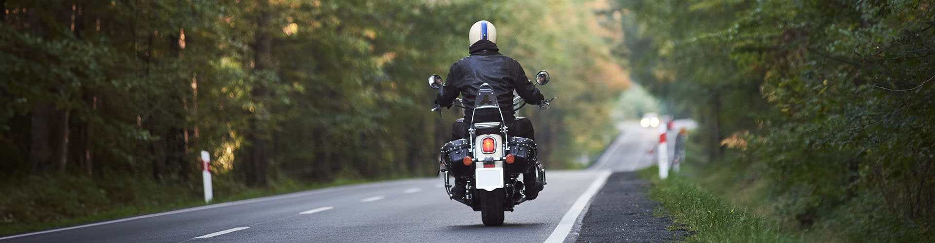 biker in black leather outfit driving modern powerful motorcycle along sunny road on summer day