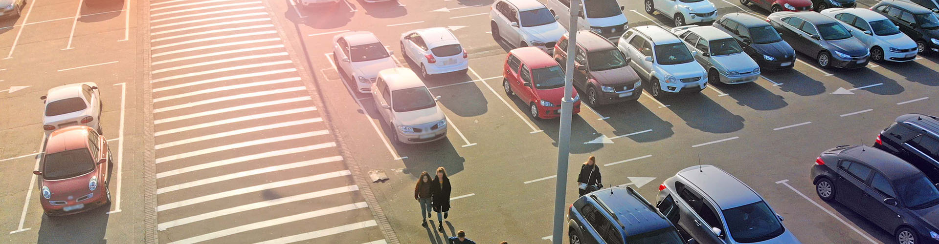 pedestrian crossing and parking lot next to the entrance of a mall. aerial. people go to the mall