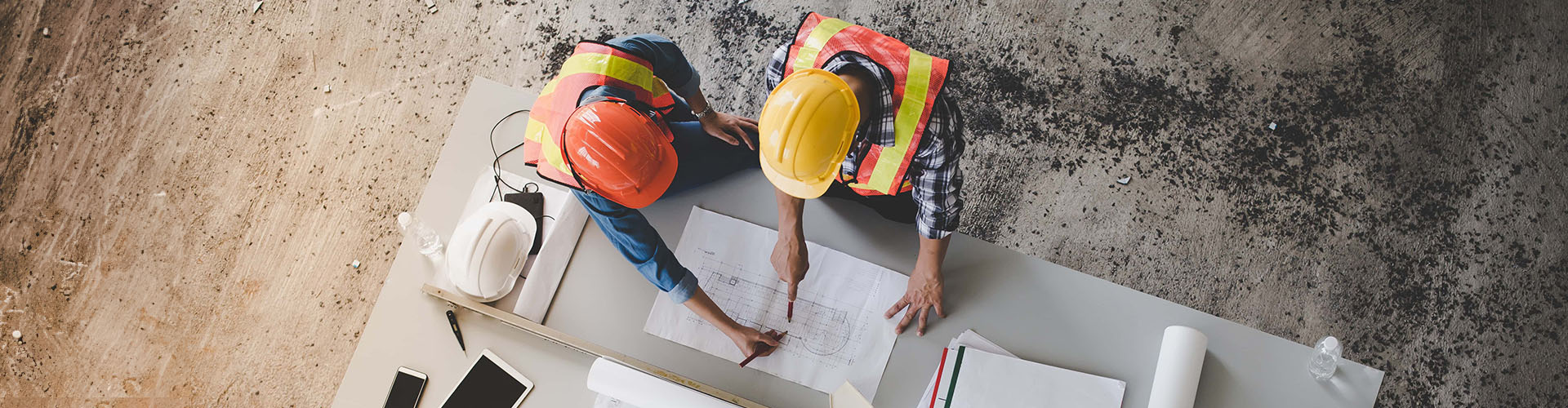 two construction workers in protective headgear reviewing blueprints at construction site - Kane County Construction Accident Lawyer concept image